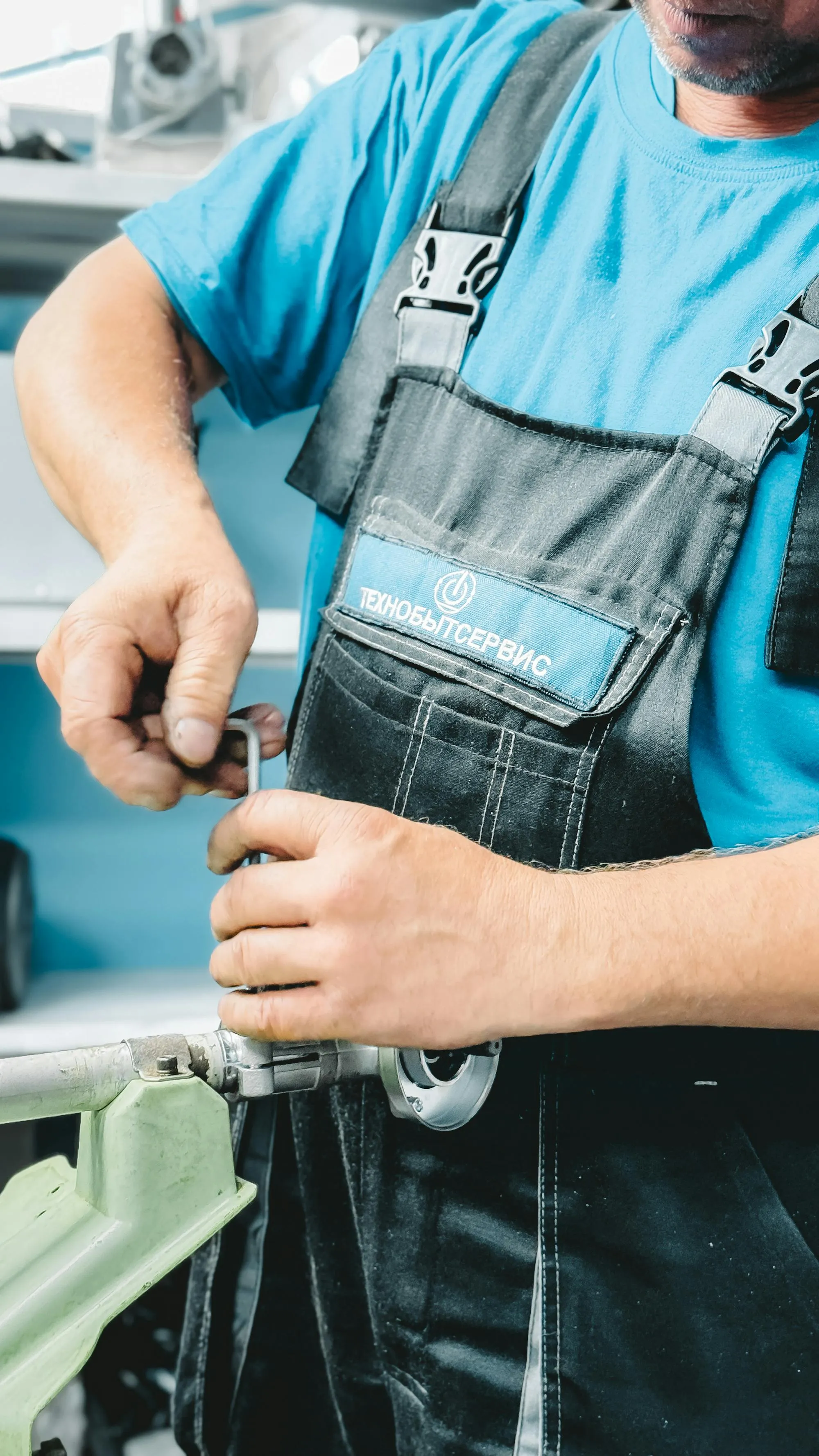 Plumber in blue overalls tightening a pressure valve with a heavy wrench